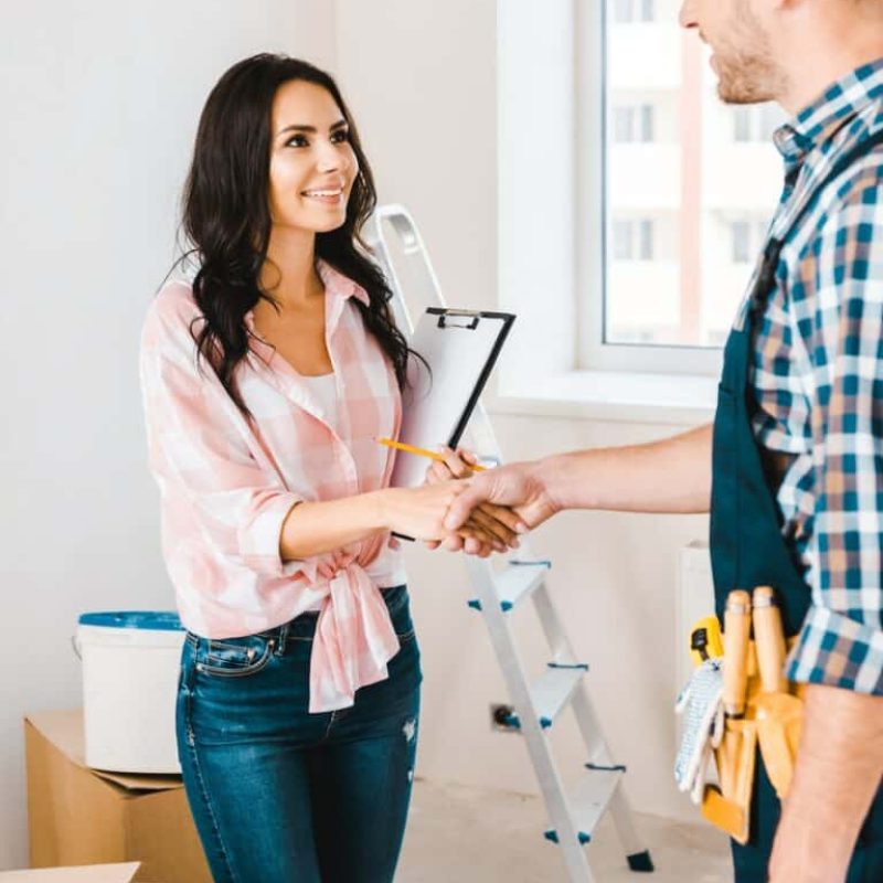 cheerful-woman-holding-clipboard-and-shaking-hands-with-handyman-768x1151
