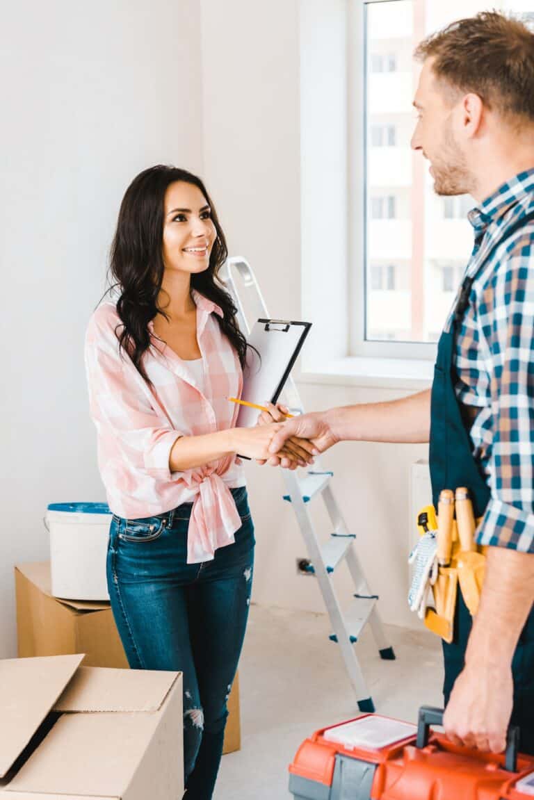 cheerful-woman-holding-clipboard-and-shaking-hands-with-handyman-768x1151